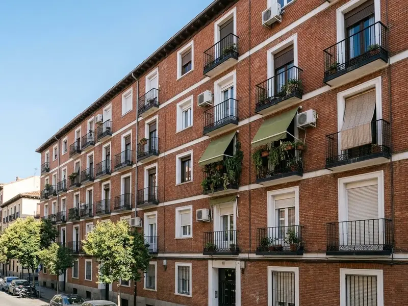 Fachada de un edificio de pisos de ladrillo en Madrid con balcones de hierro y toldos verdes